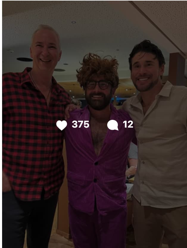 Three men posing together indoors, smiling at the camera. The man on the left wears a red plaid flannel shirt, the man in the center wears a purple velvet suit with a curly brown wig and glasses, and the man on the right wears a light beige button-up shirt. A social media overlay shows 375 likes and 12 comments.