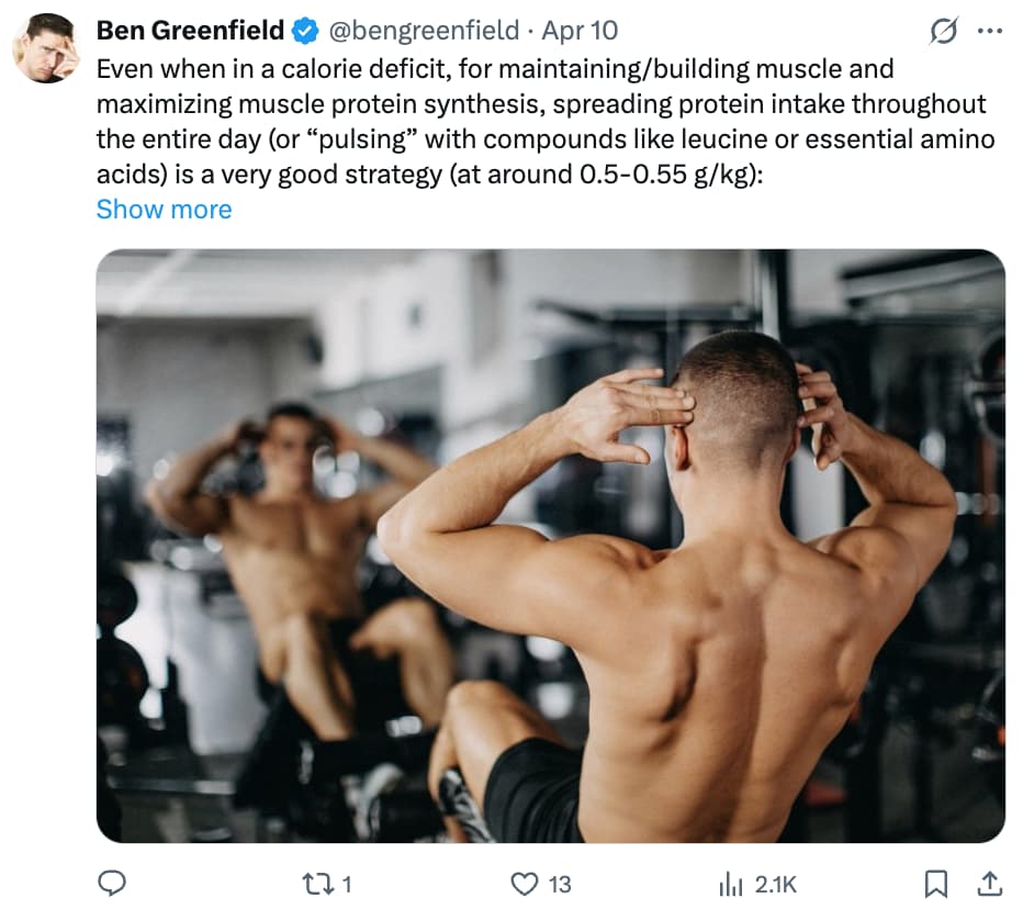 Screenshot of a tweet by Ben Greenfield (@bengreenfield), verified with a blue checkmark, posted April 10. The tweet reads: "Even when in a calorie deficit, for maintaining/building muscle and maximizing muscle protein synthesis, spreading protein intake throughout the entire day (or 'pulsing' with compounds like leucine or essential amino acids) is a very good strategy (at around 0.5–0.55 g/kg): [Show more]." Below the text is a photo of a muscular shirtless man with a close-cropped haircut, seen from behind, with both hands clasped behind his head, sitting in a gym with equipment and a mirror visible in the background. The tweet shows 0 replies, 1 retweet, 13 likes, and 2,100 views.