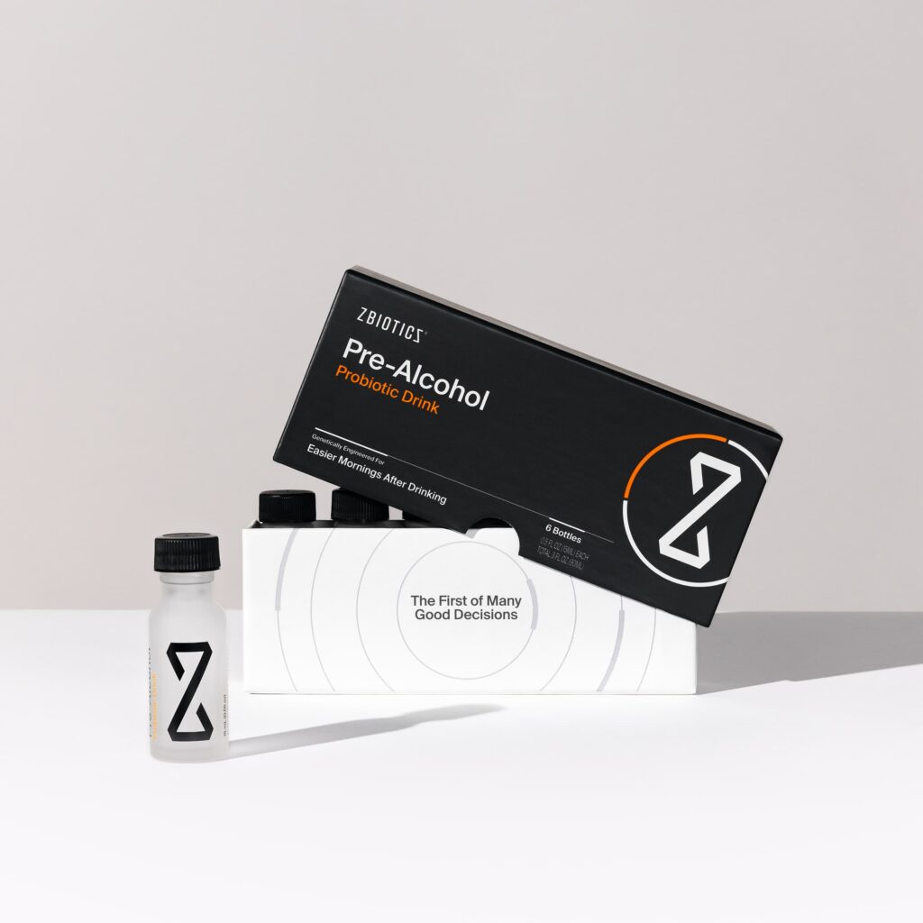ZBiotics Pre-Alcohol Probiotic Drink 6-bottle packaging displayed against a light gray background, featuring a black outer box with orange accent text and the ZBiotics logo, a white inner tray reading 'The First of Many Good Decisions,' and a single small frosted shot bottle placed in front.